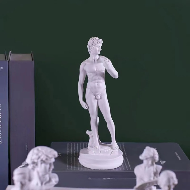0-247308.png Statue blanche d'un homme nu . A côté il y aun livre et 2 petites sculpture aux pieds