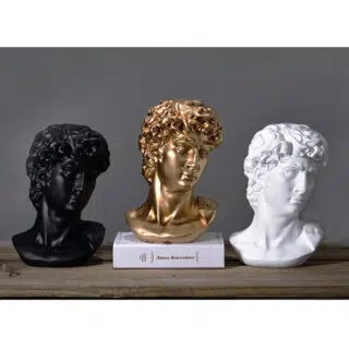 Photo de trois statues têtes d'Apollon une noire, une dorée sur un livre blanc et une blanche le tout sur fond gris