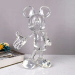 Sur fond gris, on voit une statue de Mickey Mouse en résine transparente, qui ressemble à du verre.