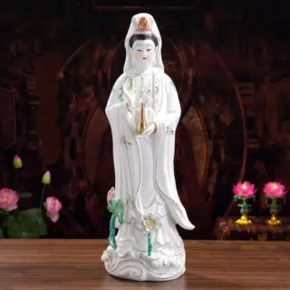 Photo d'une statue de bouddha blanche en porcelaine avec des fleurs colorées sur le piédestal le tout sur fond noir
