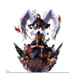 Photo d'une statue de Konan avec ses ailes d'ange surmontant Pain elle porte un grand manteau noir à nuage rouge et lui également avrc un pantalon bleu foncé bandeau dans ses chaveux rouge et piercings sur le visage et les bras sur un socle comme de la lave le tout sur fond blanc
