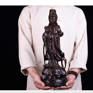 Photo d'un homme en chemise rose pale portant une statue de bouddha en bois de rose sculptée le tout sur fond noir