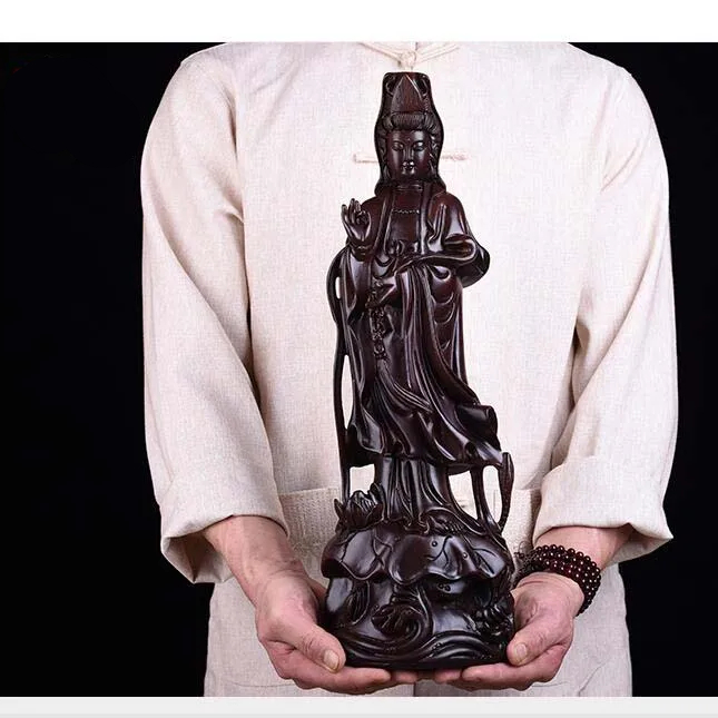 0-84d8db.jpeg Photo d'un homme en chemise rose pale portant une statue de bouddha en bois de rose sculptée le tout sur fond noir