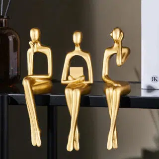 3 statuettes dorées assissent sur une étagère