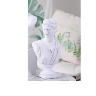 Photo d'une statue blanche buste de femme avec haut drapé sur la poitrine décolleté en V la tête tournée sur la droite sur fond de coussin blanc imprimé vert