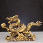 Photo d'une statue de dragon doré à cinq griffes sur socle travaillé et posé sur un meuble clair sur fond noir