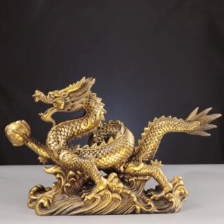 Photo d'une statue de dragon doré à cinq griffes sur socle travaillé et posé sur un meuble clair sur fond noir
