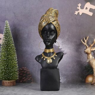 Photo d'une statue africaine d'un buste de femme portant un turban doré, des boucles d'oreilles et deux gros colliers dorés aussi l'un ras-de-cou, l'autre plastron sur un fond violine avec un arbuste à gauche