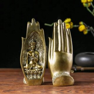 Photo d'une statue de main dorée vue de face et de dos contenant un bouddha assis en prière posée sur un meuble en bois marron