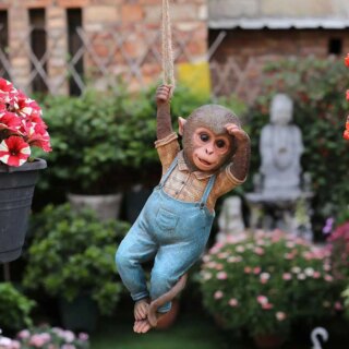 Statue de singe habillé suspendu dans un jardin.
