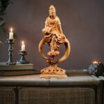Photo d'une déesse Guanyin en bois sculpté avec socle sur une table grise avec deux bougeoirs et bougies allumées en fond
