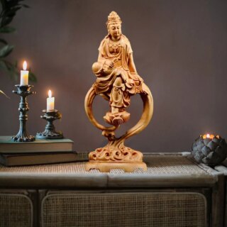 Photo d'une déesse Guanyin en bois sculpté avec socle sur une table grise avec deux bougeoirs et bougies allumées en fond