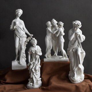 Photo de quatre statues blanches représentant les Trois Grâces de la mythologie grecques seules puis ensemble sur un tissu plissé marron et fond gris