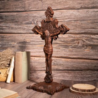 On voit une statue de Jésus sur la croix, en bois, sur socle, posée sur une surface en bois près de vieux livres.