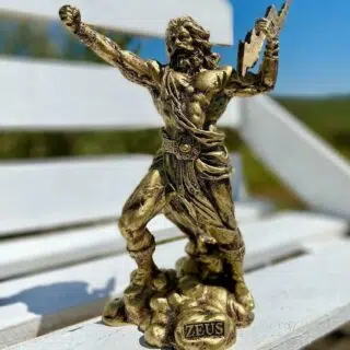 Sur un banc blanc, en extérieur, on voit une statue de Zeus, dorée, qui lève le poing au ciel et qui tient un éclair dans l'autre main. Il s'apprête à partir en guerre.