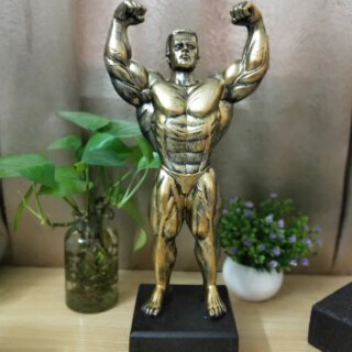 On voit une statue dorée représentant Hercule qui pose comme un bodybuildeur, en slip, avec ses muscles saillants.