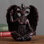 Sur un plan de travail en bois, près de deux livres reliés, on voit une statue noire en résine représentant Baphomet.