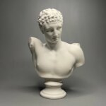 Photographie d'une statue de buste d'Hermès blanche tête légèrement penchée sur un socle rond le tout sur fond gris