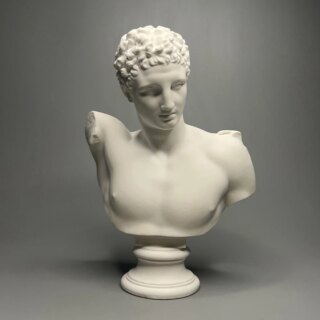 Photographie d'une statue de buste d'Hermès blanche tête légèrement penchée sur un socle rond le tout sur fond gris