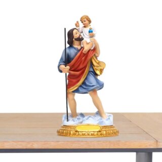 Photo de Saint Joseph debout jambes écartées tenant son bâton dans la main droite et portant l'enfant Jésus sur son épaule, il est vêtu d'une robe courte bleue et d'une étoffe rouge et dorée dessus ,l'enfant porte une robe blanche et un globe crucifère bleu dans sa main,socle doré ovale les pieds comme dans un nuage blanc le tout posé sur une table en bois et fond blanc