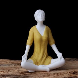 Photo d'une statue de femme stylisée en position yoga du lotus vêtue d'une robe jaune assise sur un tapis le tout sur fond noir