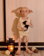 Statue Harry Potter Dobby tenant une chaussette placé à côté d'une petite lampe à huile