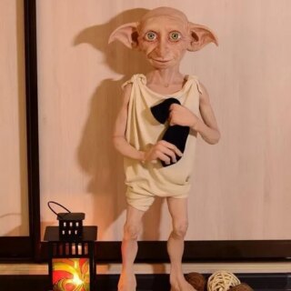 Statue Harry Potter Dobby tenant une chaussette placé à côté d'une petite lampe à huile