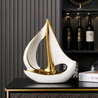 Photo d'une statue de voilier blanc et doré stylisé posé sur un meuble foncé avec des bouteilles de vin en arrière plan