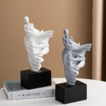 Photographie de deux statues contemporaines de femmes stylisées portant une étoffe qui s'envole d'in côté en faisant de jolis plis, une statue blanche et l'autre grise sur socle noir