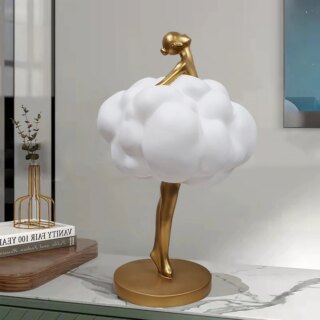 Photographie d'une statue représentant une jeune femme dorée dans un nuage blanc en train de danser la tête relevée le tout sur un socle rond lui-même posé sur un meuble style marbre