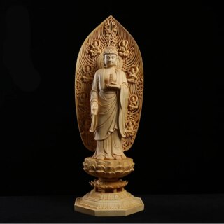 Photographie d'une statue en bois sculpté de bouddha debout sur un piédestal avec un dos ovale haut le tout sur fond noir