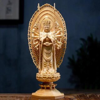 Photographie d'une statue de bouddha aux mille mains en bois sculpté sur piédestal et grand paravent ovale au dos le tout sur fond noir