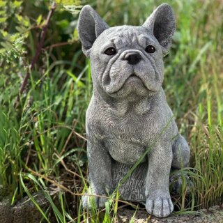 On voit une statue de Bouledogue français posée dans l'herbe.