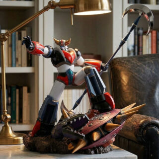 Cette statue Goldorak triomphant d'un golgoth représente le célèbre robot géant brandissant sa hache devant un fauteuil en cuir, avec une bibliothèque en arrière-plan. La figurine colorée écrase un ennemi mécanique sous son pied dans une pose de victoire héroïque.